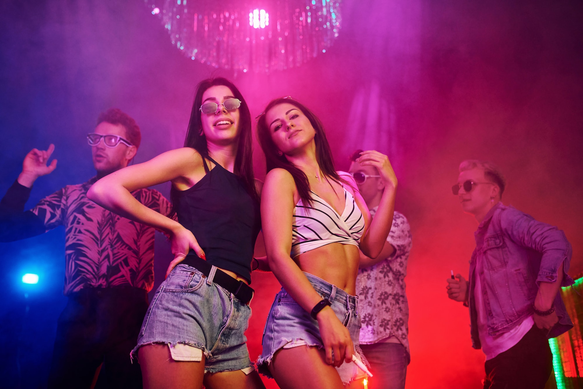 Two beautiful girls dancing in front of young people that having fun in night club